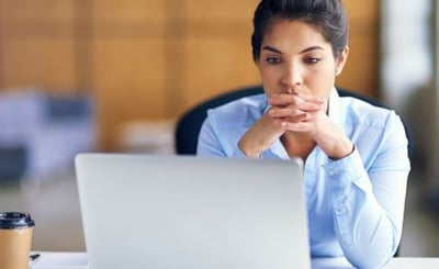 Woman looks at computer with hands folded